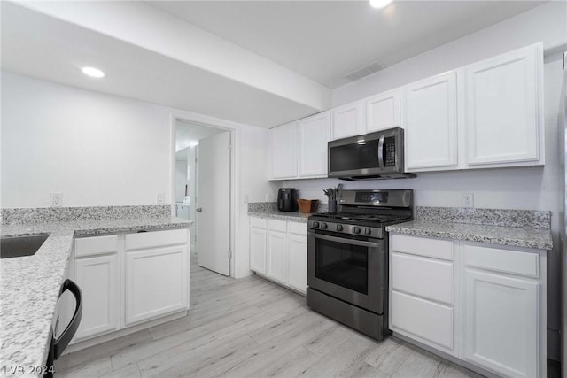 kitchen with appliances with stainless steel finishes, light stone counters, white cabinets, and light hardwood / wood-style floors