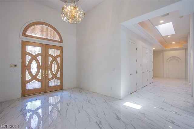 tiled entrance foyer with a raised ceiling, french doors, and a chandelier