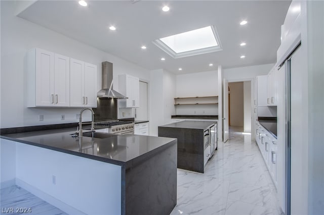 kitchen with a skylight, stainless steel range, light tile patterned floors, wall chimney range hood, and white cabinets