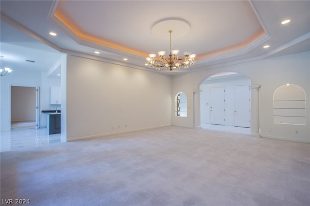 carpeted spare room with a notable chandelier, ornate columns, and a raised ceiling