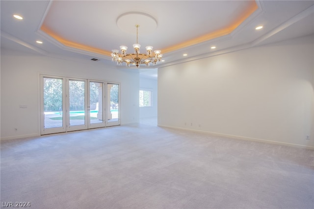 carpeted spare room featuring plenty of natural light, a chandelier, and a tray ceiling