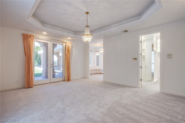 carpeted spare room featuring crown molding, a raised ceiling, french doors, and a notable chandelier