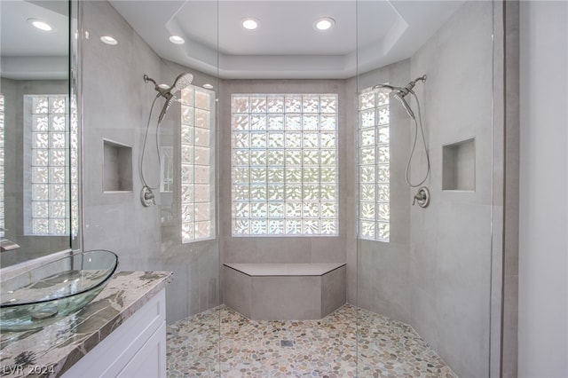 bathroom with vanity, a tile shower, a raised ceiling, and tile walls