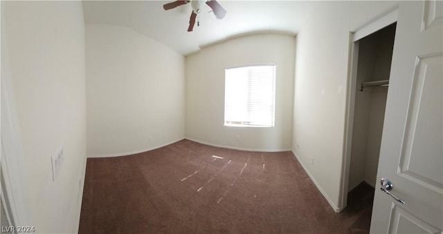 unfurnished bedroom with ceiling fan, vaulted ceiling, a closet, and dark colored carpet