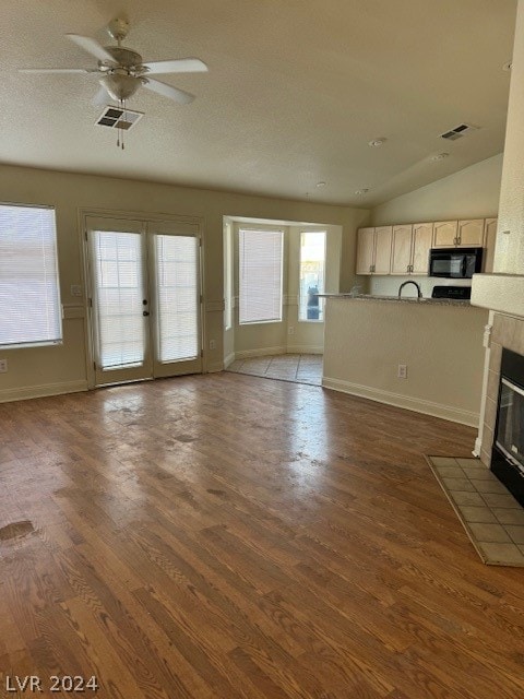 unfurnished living room featuring hardwood / wood-style floors, french doors, a tiled fireplace, lofted ceiling, and ceiling fan