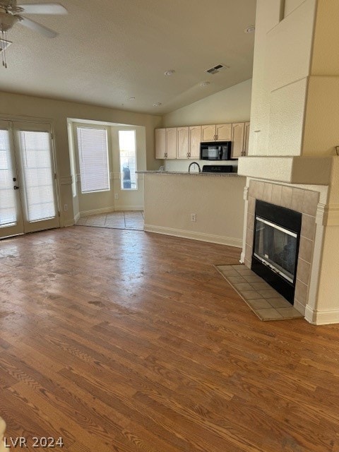 unfurnished living room featuring lofted ceiling, ceiling fan, wood-type flooring, and a tile fireplace