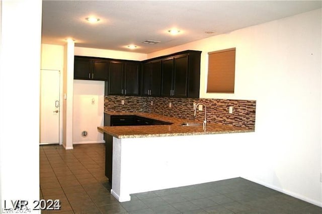 kitchen with kitchen peninsula, decorative backsplash, dark tile patterned flooring, light stone counters, and sink