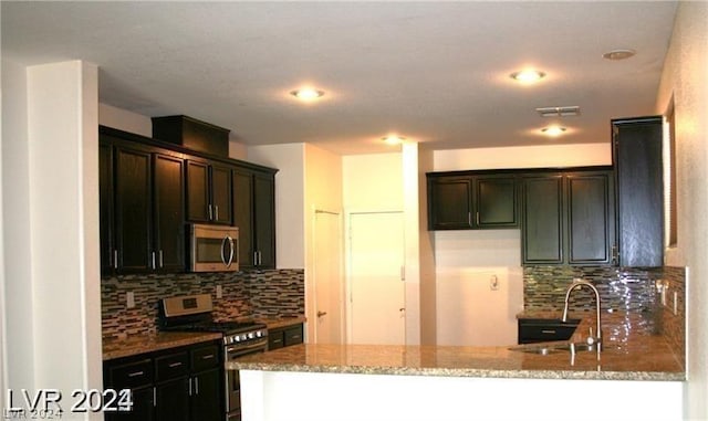 kitchen featuring stainless steel appliances, sink, backsplash, kitchen peninsula, and light stone counters