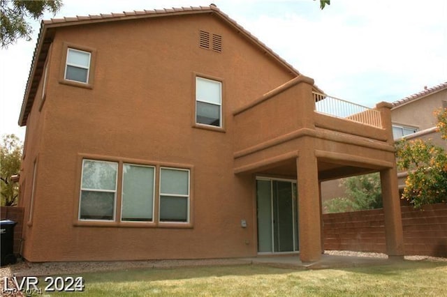 rear view of house featuring a balcony and a yard