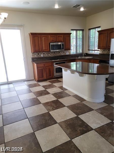 kitchen with a kitchen breakfast bar, a wealth of natural light, appliances with stainless steel finishes, and backsplash