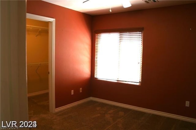 unfurnished bedroom with ceiling fan, a closet, a spacious closet, and carpet flooring