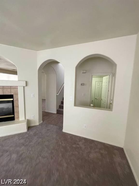 unfurnished living room with dark carpet and a tiled fireplace