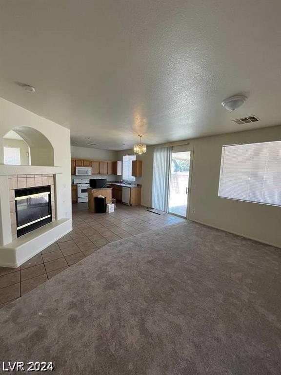 unfurnished living room with a textured ceiling, light tile patterned floors, and a tiled fireplace