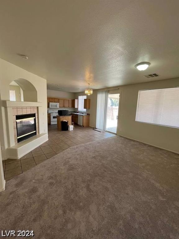 unfurnished living room with a chandelier, a tiled fireplace, a textured ceiling, and dark colored carpet