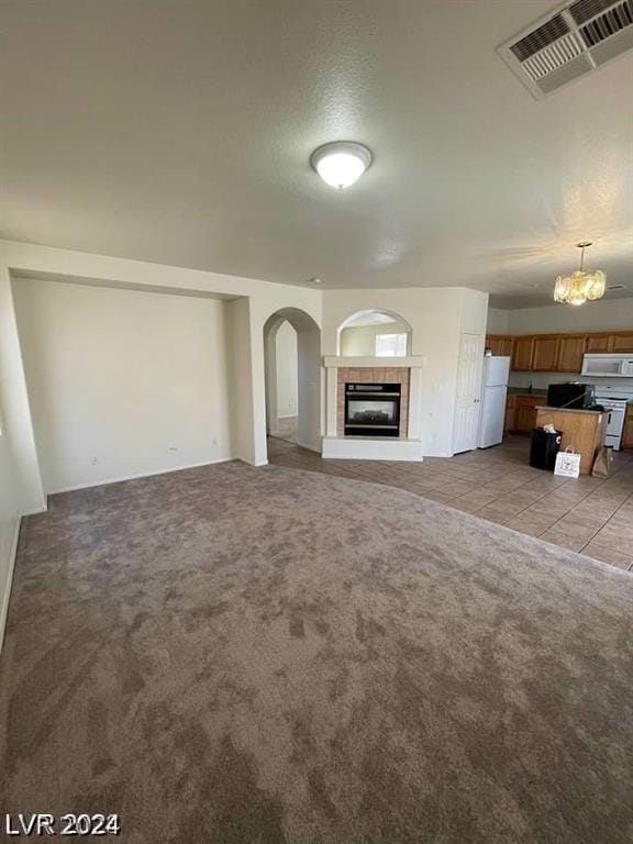 unfurnished living room featuring light carpet, an inviting chandelier, and a tile fireplace