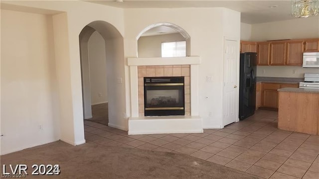 kitchen featuring a tiled fireplace, light colored carpet, stove, and black fridge with ice dispenser