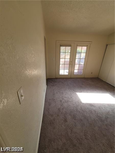 unfurnished room with a textured ceiling, carpet floors, and french doors