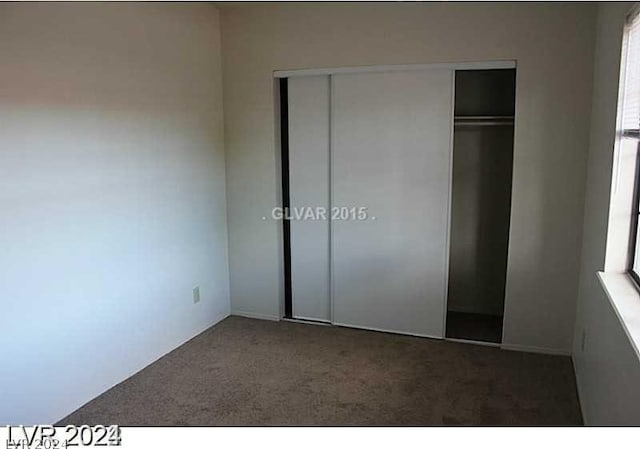 unfurnished bedroom featuring a closet, dark carpet, and multiple windows