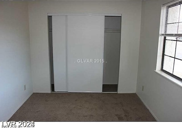 unfurnished bedroom featuring dark carpet, multiple windows, and a closet