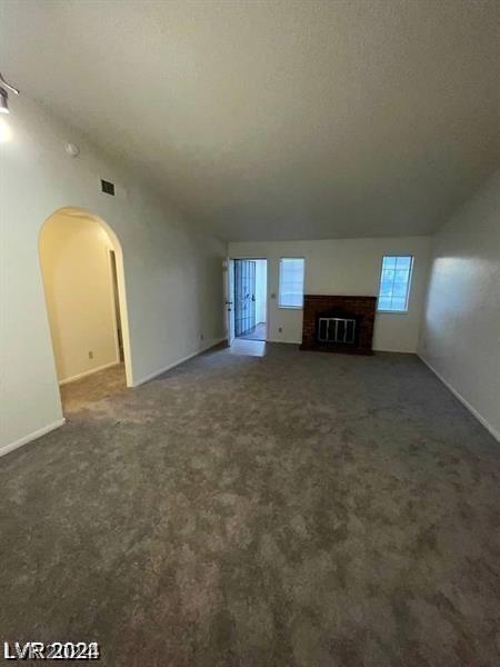 unfurnished living room with vaulted ceiling, a brick fireplace, and dark colored carpet