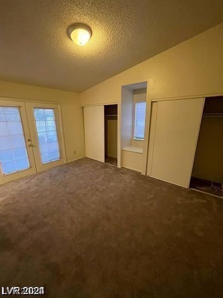 unfurnished bedroom with french doors, vaulted ceiling, a textured ceiling, and dark carpet