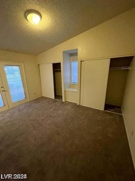 unfurnished bedroom with multiple closets, vaulted ceiling, dark carpet, and a textured ceiling