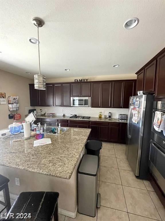 kitchen featuring hanging light fixtures, a kitchen island with sink, a kitchen breakfast bar, stainless steel appliances, and light tile patterned floors