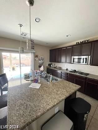 kitchen featuring hanging light fixtures, light stone counters, stainless steel appliances, and a center island with sink