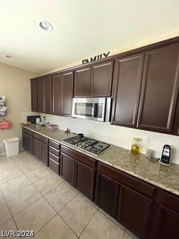 kitchen featuring light tile patterned flooring, appliances with stainless steel finishes, light stone counters, and dark brown cabinetry