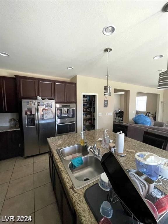 kitchen with stainless steel appliances, light tile patterned flooring, dark brown cabinets, light stone counters, and sink