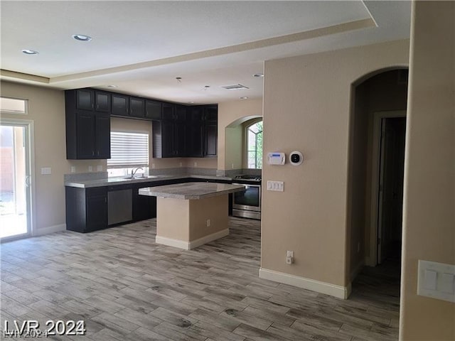 kitchen with a kitchen island, stainless steel appliances, sink, a tray ceiling, and light hardwood / wood-style flooring