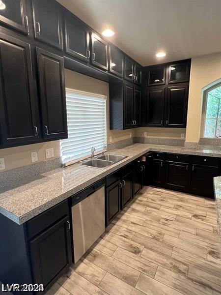 kitchen with light stone countertops, stainless steel dishwasher, and sink