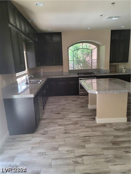 kitchen with sink, light stone counters, and stainless steel gas range oven