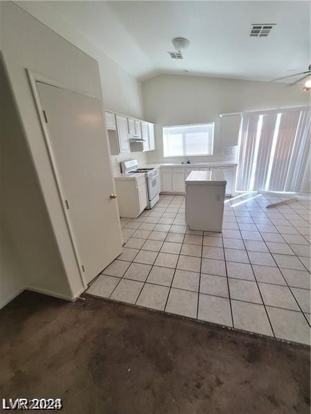 kitchen with vaulted ceiling, a kitchen island, gas range gas stove, light tile patterned flooring, and white cabinets