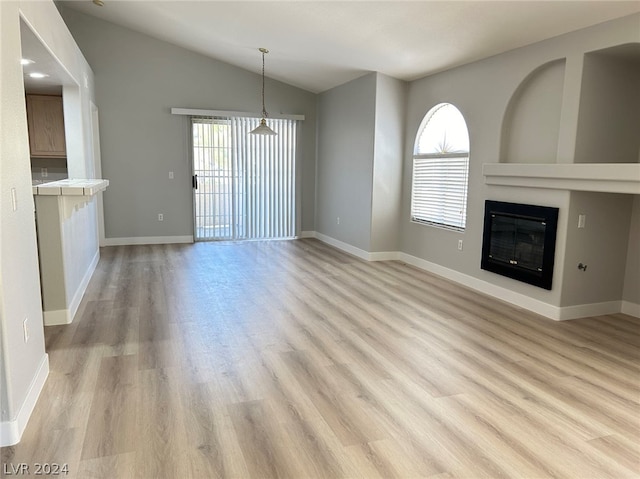 unfurnished living room with a chandelier, lofted ceiling, and light hardwood / wood-style floors