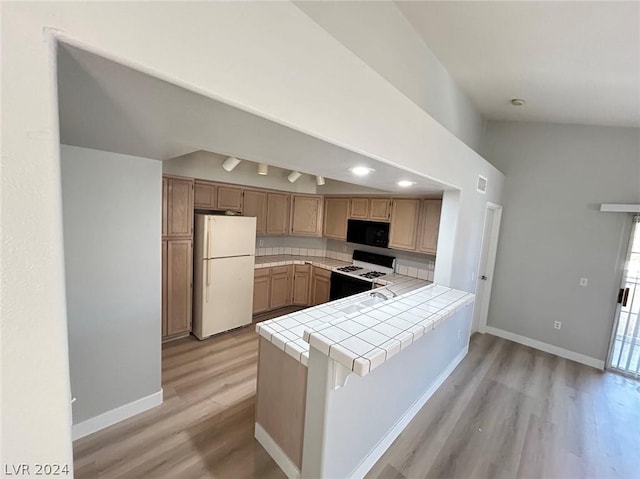 kitchen with white appliances, light wood-style floors, a peninsula, baseboards, and tile counters