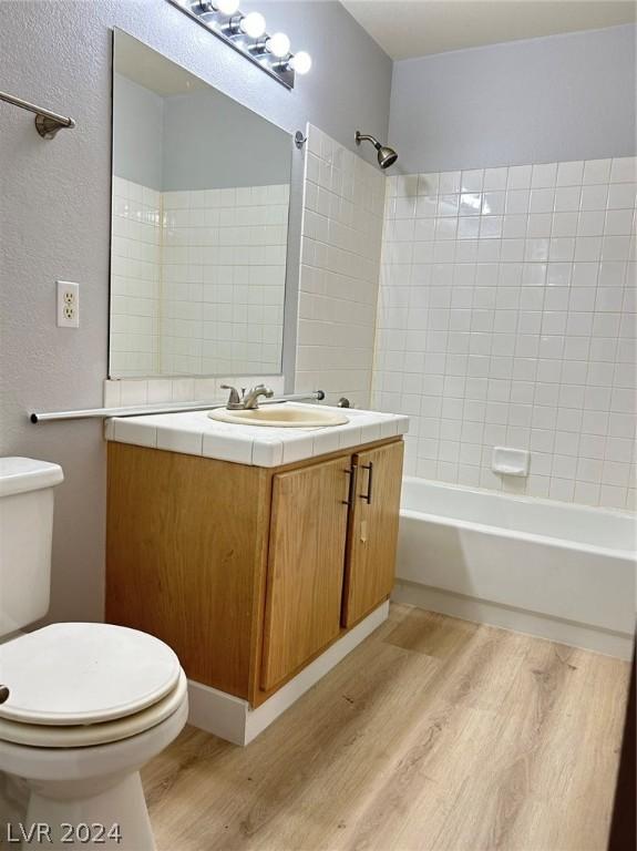 bathroom featuring toilet, wood finished floors, bathtub / shower combination, a textured wall, and vanity