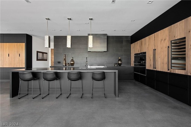 kitchen featuring a breakfast bar, a large island with sink, sink, hanging light fixtures, and concrete flooring