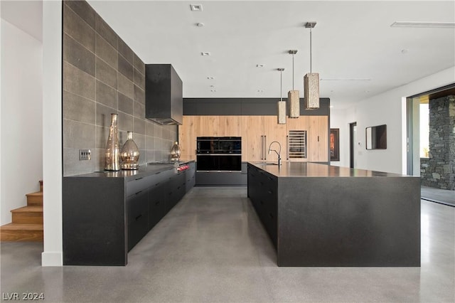 kitchen featuring sink, hanging light fixtures, stainless steel gas cooktop, black double oven, and a kitchen island with sink