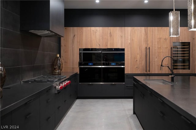 kitchen featuring double oven, sink, decorative light fixtures, wine cooler, and stainless steel gas stovetop