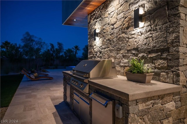 patio at twilight featuring a grill and exterior kitchen