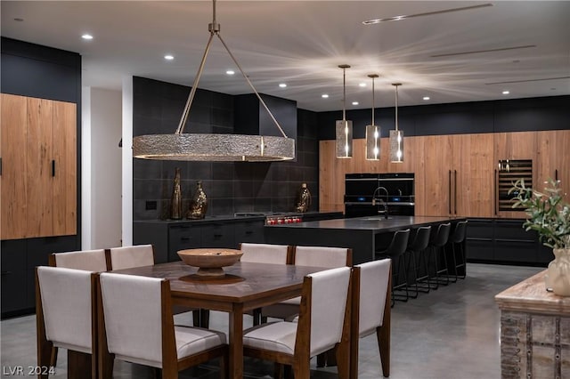 bar featuring sink, wall chimney range hood, double oven, concrete flooring, and decorative light fixtures