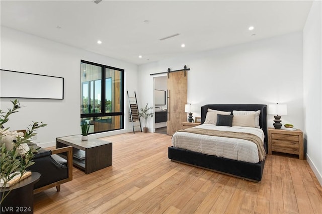 bedroom featuring a barn door, light hardwood / wood-style floors, and connected bathroom