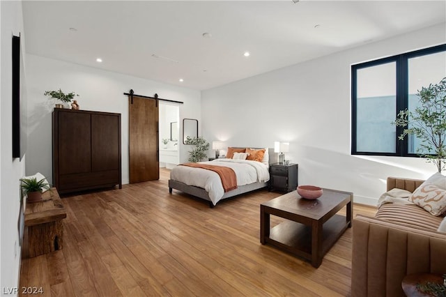 bedroom with a barn door, ensuite bath, and light hardwood / wood-style floors