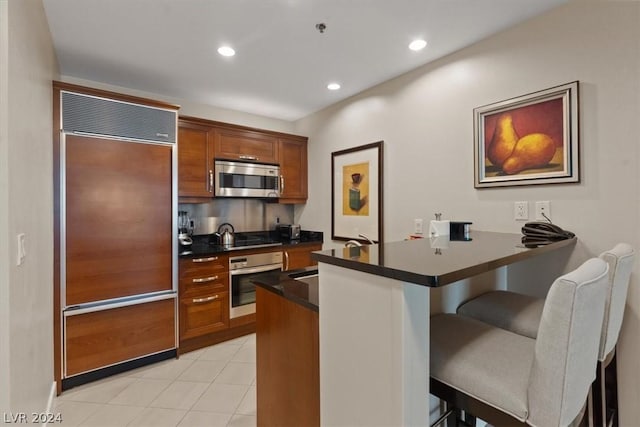 kitchen featuring stainless steel appliances, light tile patterned flooring, a breakfast bar, and kitchen peninsula