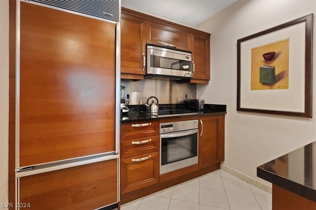 kitchen featuring stainless steel appliances, dark countertops, brown cabinets, light tile patterned floors, and baseboards