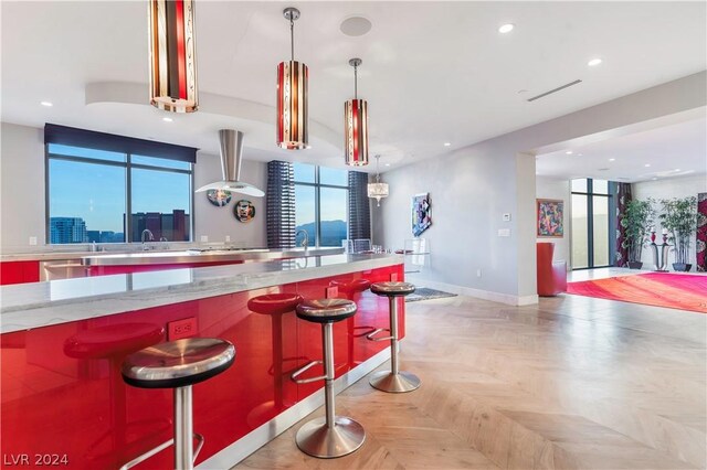 kitchen with light parquet floors, decorative light fixtures, dishwasher, and a kitchen bar