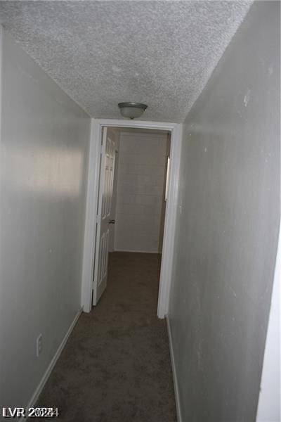 hall with a textured ceiling and dark carpet