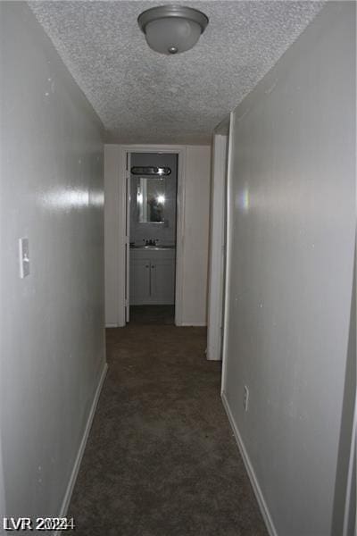 corridor featuring a textured ceiling and dark colored carpet