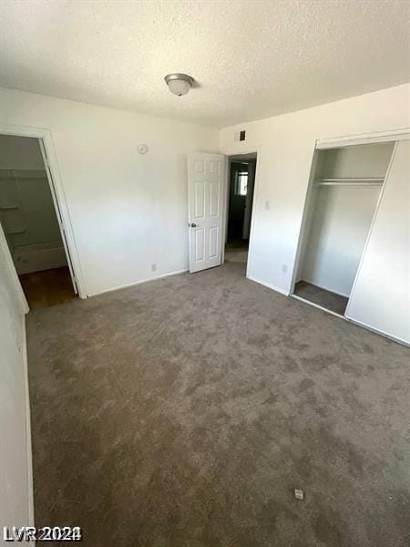 unfurnished bedroom featuring a textured ceiling, a closet, and dark colored carpet